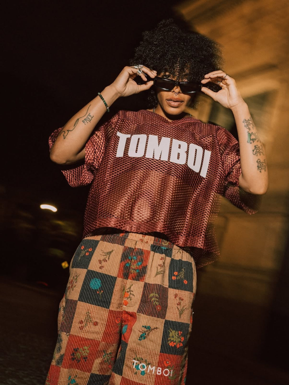 Person wearing maroon TOMBOI jersey with patterned pants at night